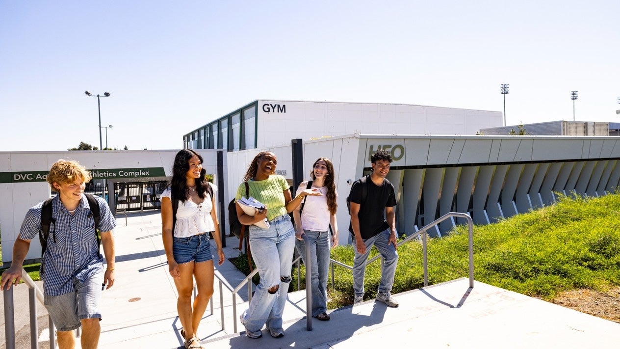 Five students walk and talk together outside the DVC Aquatics and Athletics Complex on a sunny day.