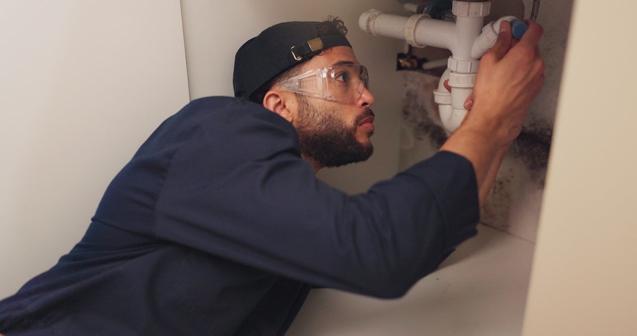 A male plumber works on fixing a pipe