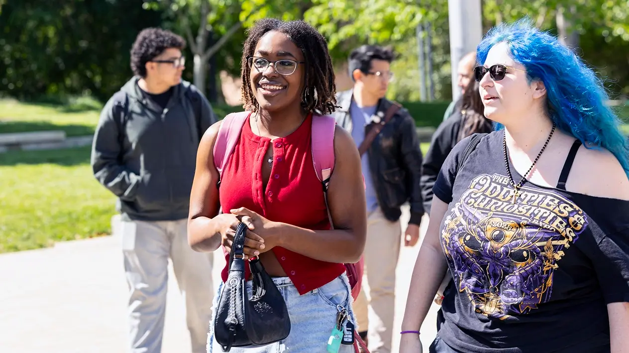 Two female students in the forefront walking the DVC campus with two guys behind them also walking. All conversating amongst each other.