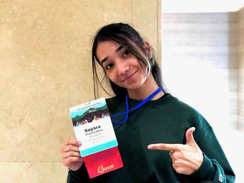Sayara Rozymuradova holding and pointing to her student leadership name badge.
