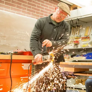 Construction professor using a tool to saw a metal component on a workbench