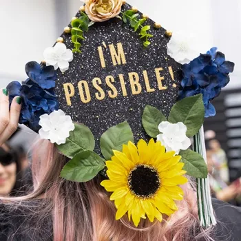 Female graduate wearing a graduation cap, with sunflowers and decorated green leafs, saying the wording: "It's Possible!"