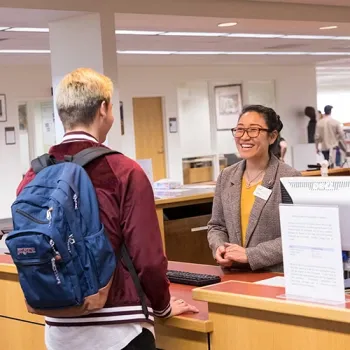 Librarian standing behind desk, helping approaching student.