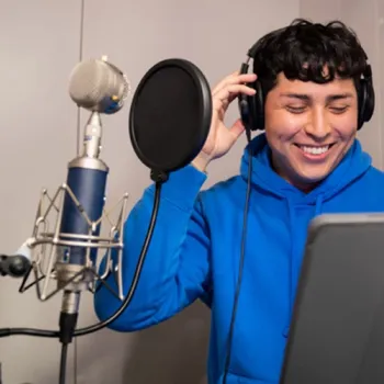 Student wearing headphones, standing at the microphone, smiling and singing