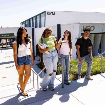Five students walk and talk together outside the DVC Aquatics and Athletics Complex on a sunny day.