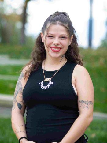 Smiling student with tattoos and facial piercings stands outdoors on campus.